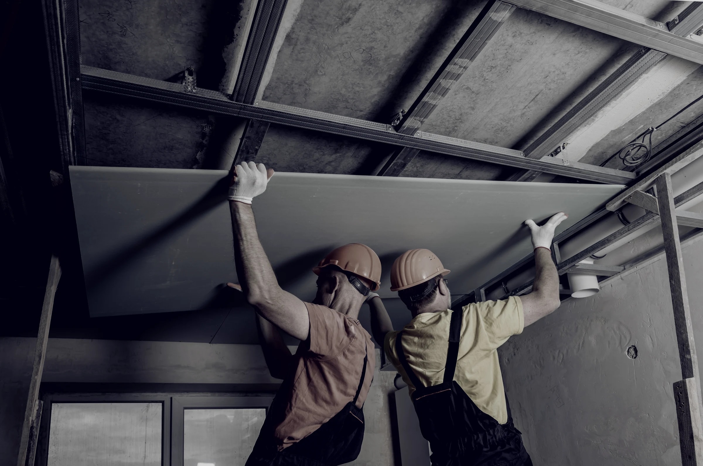 Two installers lifting a board into a suite ceiling grid